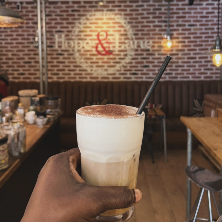 A person holding up their coffee inside Hope & Lane coffee shop, Deal