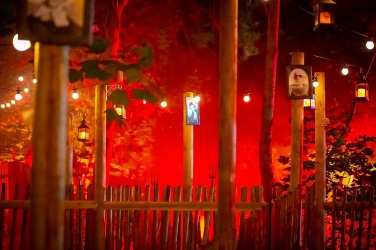 An image of spooky woods lit up in red light with lanterns leading the way along a trail
