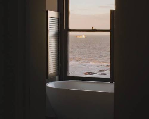 An image of a bathtub situated next to a window with views of the sea
